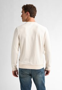 Crèmekleurige sweatshirt met een gestructureerde afwerking, ronde hals en ribgebreide manchetten. Draagt met blauwe spijkerbroek, toont een casual achterkant.
