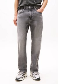 Person wearing grey straight-leg jeans, black t-shirt, and white running shoes standing against a white background.