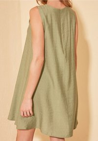 Grünes ärmelloses Kleid aus strukturiertem Stoff, mit lockerem Schnitt und einer hinteren Naht mit einem kleinen Verschluss. Leicht ausgestellt am Saum.