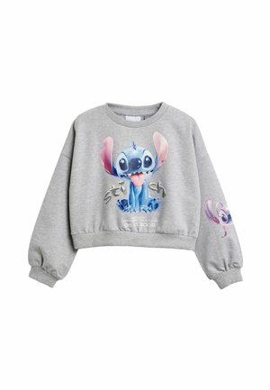 Sweat-shirt court gris clair avec un personnage de dessin animé bleu ludique, aux grandes oreilles et la langue tirée, imprimé sur le devant et la manche.