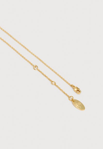 Trapių auksinių grandinėlės pakabukas su ovaliu užsegimu ir mažame ovaliame pakabuke ant kurio išgraviruotas logotipas baltame fone.