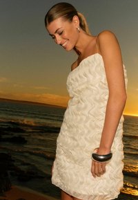 Robes blanches à volants en tissu texturé, avec des bretelles fines et une silhouette fluide. Avec un bracelet métallique au poignet.