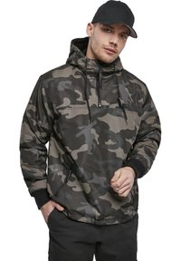 Chaqueta de camuflaje en tonos de gris y negro, con capucha, bolsillo frontal tipo pouch y cordón ajustable. Material texturizado y ligero.