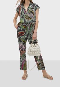 Jumpsuit multicolore con motivo floreale, scollo a V, maniche corte e vita con cordoncino, abbinato a una borsa bianca con texture e sandali.