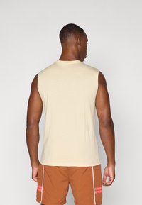 Lys beige ermeløs skjorte med rund hals, glatt tekstur og avslappet passform, kombinert med brune shorts med rosa detaljer.