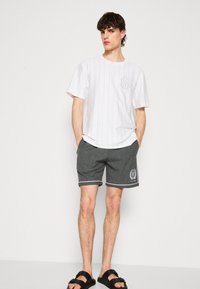 Hvit kortermet skjorte med vertikale striper og et grått tall på brystet, sammen med grå stripeshorts og svarte sandaler.