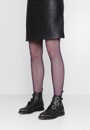 Jambes portant des collants résille noirs, une jupe en cuir noire et des bottines noires avec trois boucles argentées sur chaque botte.