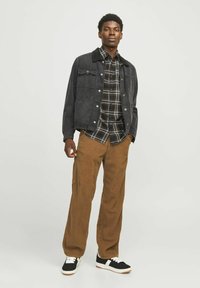 Chaqueta de mezclilla negra con un cuello suave, camisa de cuadros debajo, y pantalones de pana marrones de corte holgado combinados con zapatillas negras y blancas.