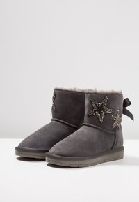 Šedé semišové kotníkové boty s umělou kožešinou uvnitř, se zdobením v podobě hvězd v metalických a kamínkových materiálech a s detailem mašle na zadní straně.