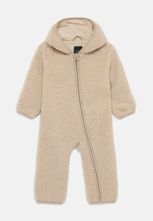 Beige fleecetakki, jossa on huppu, ja joka on varustettu täyspitkällä vetoketjulla sekä tekstuurilla varustetulla, pörröisellä kankaalla. Hihansuissa elastiset resorit.