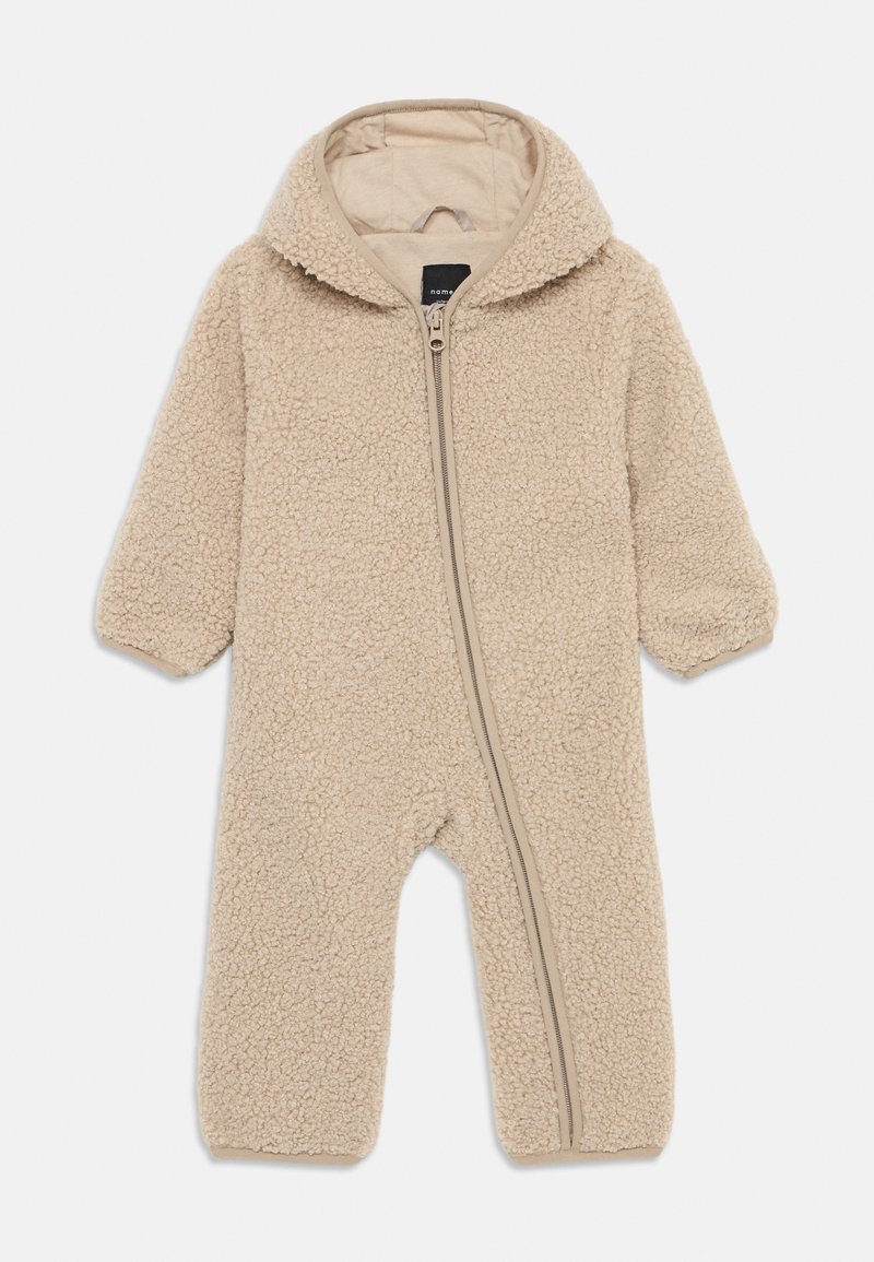 Combinaison en polaire beige avec capuche, dotée d'une fermeture éclair sur toute la longueur et d'un tissu texturé et duveteux. Poignets élastiques aux manches.