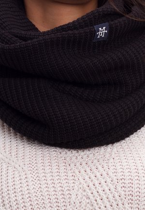 Sort strikket nakkeklud med et lille stoflogo, båret over en hvid tekstureret sweater og dækker halsen og den nedre del af ansigtet.