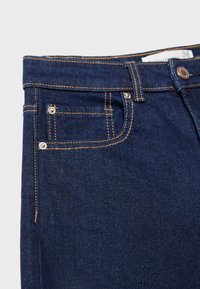 Temno modri kavbojke z klasičnim petim žepom, z kontrastnim šivanjem in kovinskim gumbom za zapiranje v pasu.