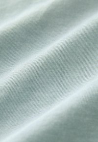 Ljust blått tyg i närbild, med en slät textur och ett fint ribbat mönster, som visar subtila variationer i färg och lyster.