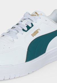 Бяла маратонка Puma с тюркоазена ивица, златно лого Puma и бели връзки на бял фон.