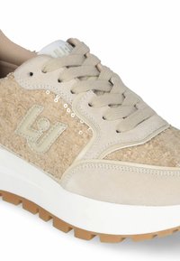 Beige tenisky s texturovaným textilním svrškem, tónovými šňůrkami a gumovou podrážkou. Na boku mají logo a dekorační flitry.