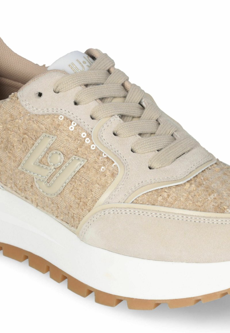 Sneaker beige con tomaia in tessuto testurizzato, lacci tono su tono e suola in gomma. Presenta un logo e paillettes decorative sul lato.
