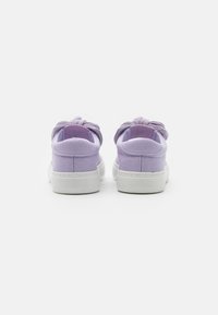 Des baskets en toile violettes avec un bout arrondi, une semelle en caoutchouc blanche et un détail en nœud au talon. La tige a une texture lisse.