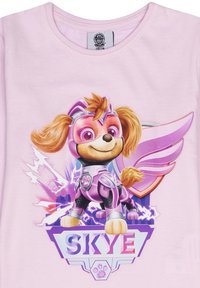 Hellblaues T-Shirt mit einem Cartoon-Hund in einem lila Superhelden-Outfit mit Flügeln. Das Design enthält den Namen "SKYE" am unteren Rand.