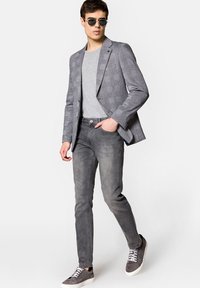 Szary w kratę marynarka na jasnoszarym T-shircie, w połączeniu z wąskimi szarymi dżinsami i szarymi sneakersami. Model nosi okrągłe okulary przeciwsłoneczne.