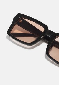 Ochelari de soare din plastic negru, cu rame pătrate și lentile nuanțate de maroniu, având un design îndrăzneț și o textură netedă.