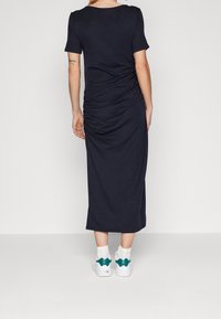 Abito blu navy, a maniche corte, lunghezza al ginocchio con dettagli arricciati sul retro, abbinato a sneakers bianche con dettagli in teal.