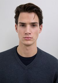 Pulover gri închis cu decolteu în V, dintr-un material moale, purtat peste o cămașă închisă la culoare. Designul prezintă o textură tradițională tricotată și o siluetă mulată.