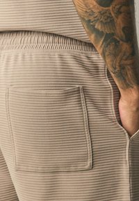 Beige ribbed shorts with an elastic waistband. Features a patch pocket on the right side and a textured fabric surface.