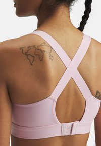 Sostén deportivo de color rosa claro con un diseño elegante, que presenta tirantes entrecruzados y una sutil marca a lo largo de los tirantes. Textura suave y cierre trasero ajustable.