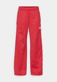 Piros melegítőnadrág, amely laza szabású, rugalmas derékpánttal, oldalsó zsebekkel és fehér csíkokkal a külső varratok mentén. Puha anyagból készült.