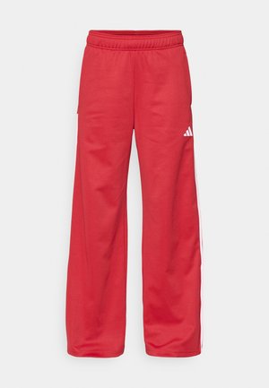 Rote Sweatpants mit entspanntem Schnitt, elastischem Bund, Seitentaschen und weißen Streifen entlang der äußeren Nähte. Hergestellt aus weichem Stoff.