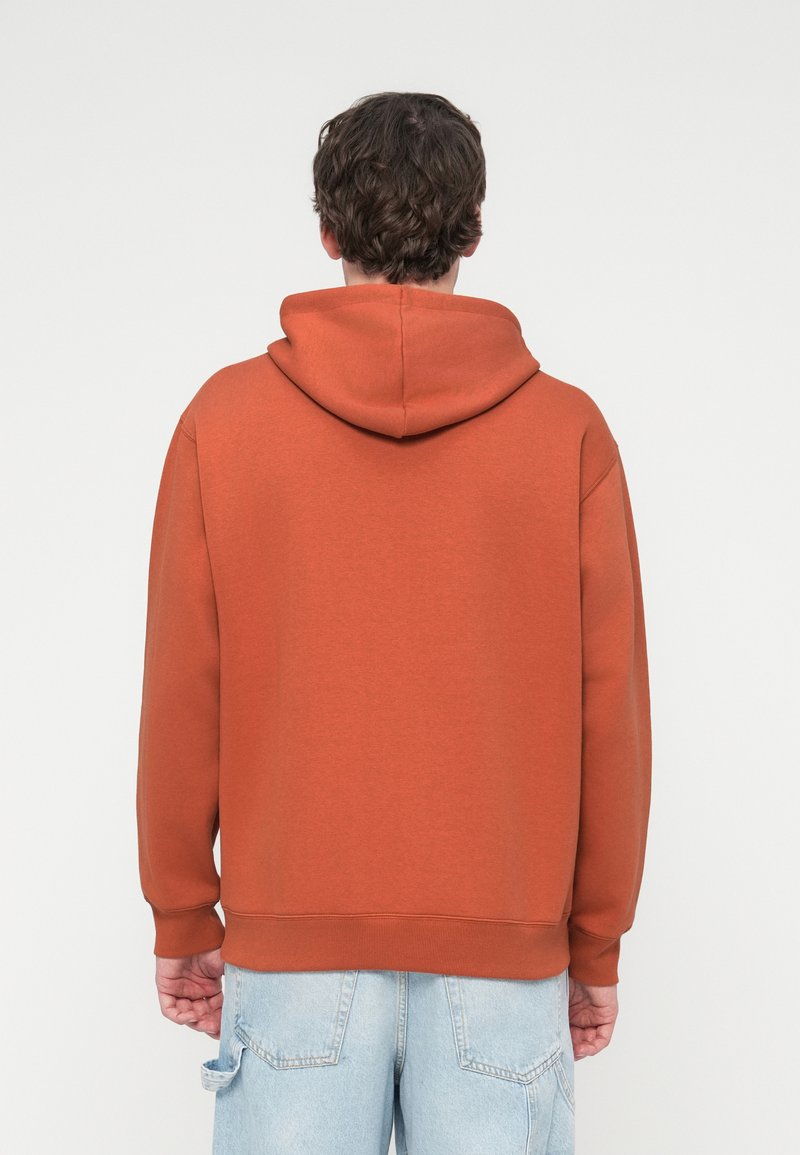 Kapuzensweatshirt in Rostfarbe aus weichem Stoff mit lockerem Schnitt und gerippten Bündchen und Saum. Rückansicht zeigt glatte Textur.