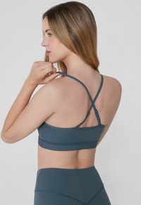 Sostenedor deportivo en tejido azul suave, con una textura lisa, diseño de espalda cruzada, tirantes ajustables y un corte entallado. Sin detalles adicionales.