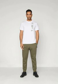 Λευκό κοντομάνικο μπλουζάκι με μαύρα γραφικά, συνδυασμένο με ελαιοπράσινες φόρμες. Το σύνολο ολοκληρώνεται με μαύρα αθλητικά παπούτσια.