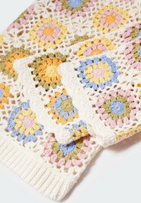 Virkat täcke med blommönster i rosa, orange, gult, grönt och blått mot en krämfärgad bakgrund med scallopkanter.