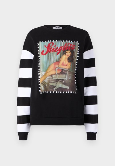 Felpa nera con maniche lunghe a righe bianche e nere. Presenta una stampa grafica di una donna seduta su una sedia, contornata di bianco.