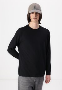 Black long-sleeve t-shirt with a crew neckline, paired with a light gray baseball cap featuring a small logo, worn with gray pants.
