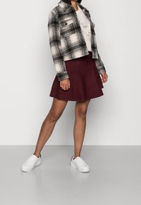 Black and white plaid cropped jacket, gray sweater with embroidery, burgundy flared skirt, and white sneakers with black detailing.