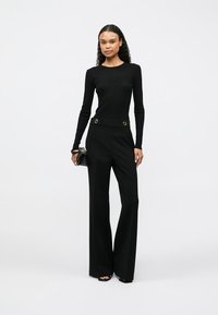 Camisola preta justa de manga longa com textura canelada, combinada com calças largas pretas de cintura alta com detalhes em dourado.