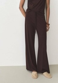 Brown wide-leg pants with a drawstring waistband, made of smooth fabric, paired with beige slip-on shoes. Simple and minimalistic design.