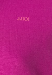 Tessuto a maglia fucsia con una superficie liscia, caratterizzato dal nome del marchio "JJXX" stampato in un tenue rosa.