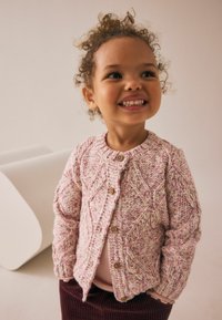 Handgehaakte cardigan in roze en crème, met een getextureerd ruitpatroon, houten knopen en geribde mouwen. G gedragen over een licht top.