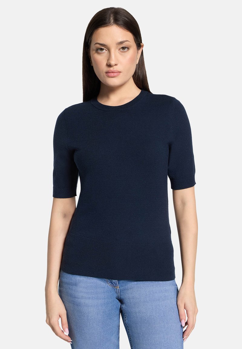 Námornícka modrá pletená blúzka s krátkym rukávom, okrúhlym výstrihom, hladkou textúrou a priliehavým strihom, v kombinácii so svetlomodrými džínsami.