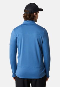 Blaues Langarmhemd mit texturiertem Muster, hohem Kragen und flachen Nähten. Verfügt über einen schwarzen Logozuschuss am Ärmel.