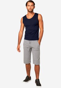 Camisetta senza maniche blu navy, pantaloni corti grigi. La canotta è aderente, senza maniche e realizzata in un tessuto liscio. I pantaloni corti hanno una cintura elastica e tasche laterali.