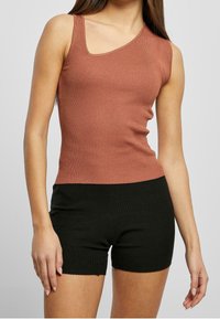 Ripp-Tanktop in Rostfarbe mit einem schulterfreien Design, kombiniert mit schwarzen, hochgeschnittenen Ripp-Shorts.