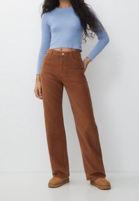 Bruna kordflortbyxor med rak passform, hög midja och framfickor, parat med en ljusblå ribbad crop top. Tan skor synliga.