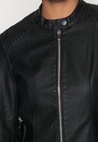 Svart läderjacka med hög krage, ribbade axelkonturer, blixtlås framtill och sidofickor med dragkedja.