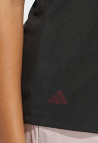 Canotta sportiva nera con un motivo testurizzato, dettagli in rete e logo Adidas bordeaux sul lato inferiore.