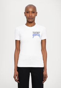 Baltas prigludęs marškinėliai su "Versace Jeans Couture" grafika mėlyna ir juoda spalvomis kairėje krūtinės pusėje. Trumpomis rankovėmis ir lygiomis tekstūra.